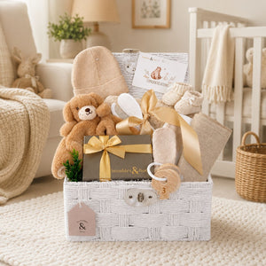 Newborn baby gifts basket with teddy bear, hat, and other items in a white hamper