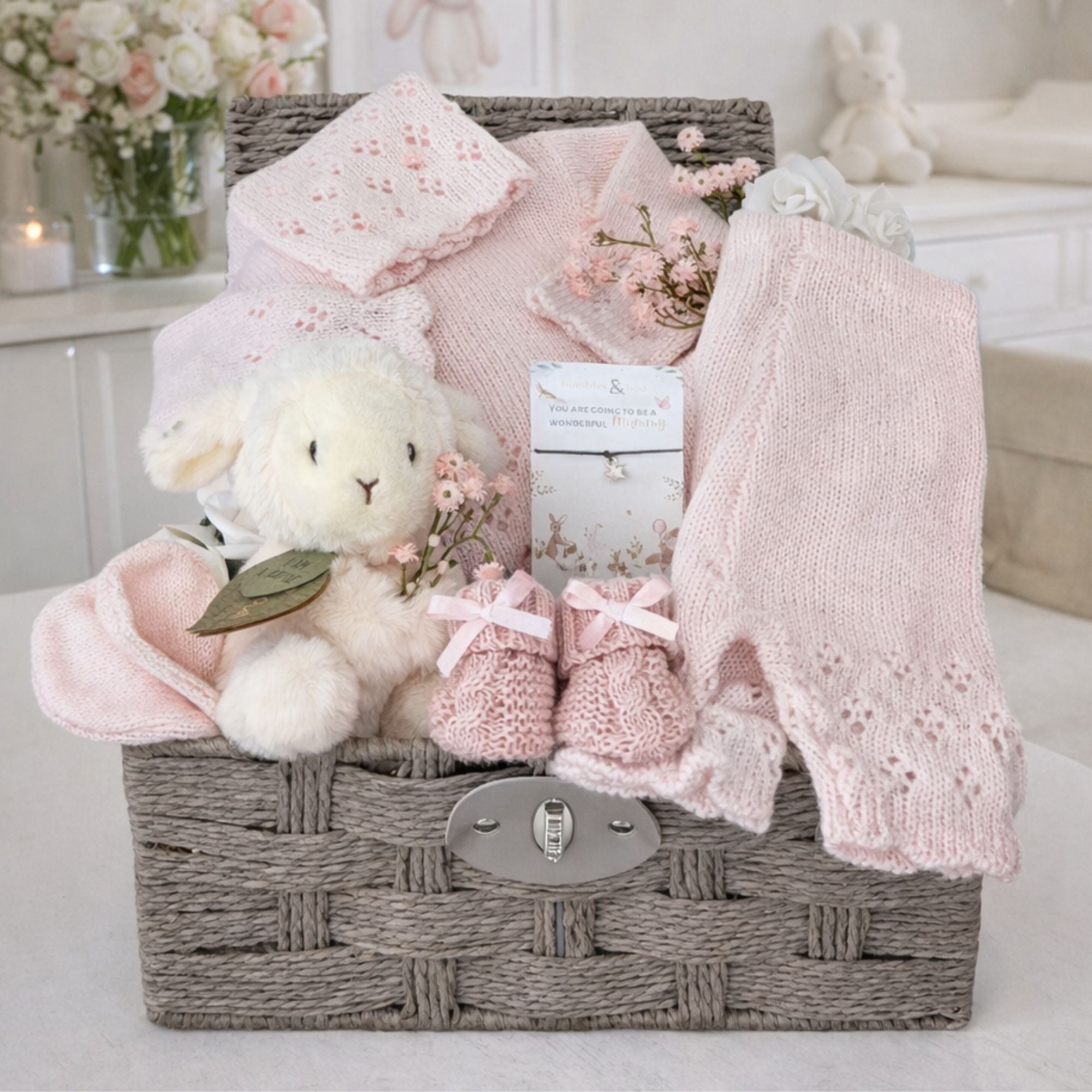 Baby girl hamper basket packed with gifts to welcome a new baby girl with pink knit clothing and a cuddly lamb.