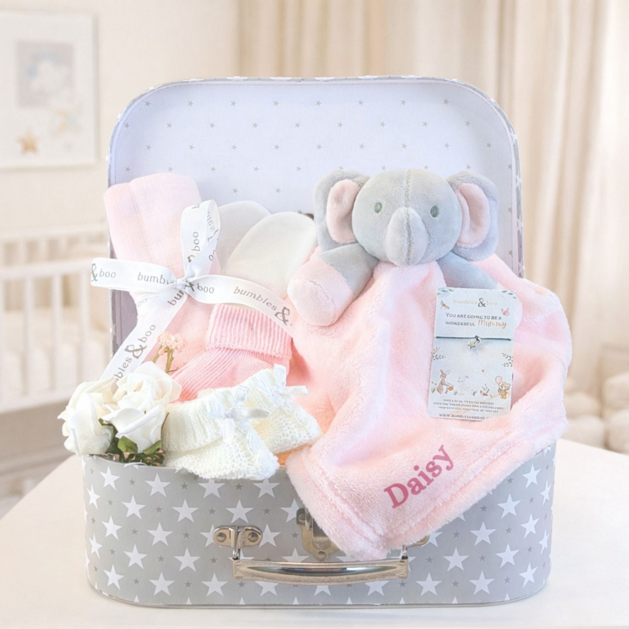 Gifts hamper for a baby girl with pink elephant soft toy and baby clothing in a box.
