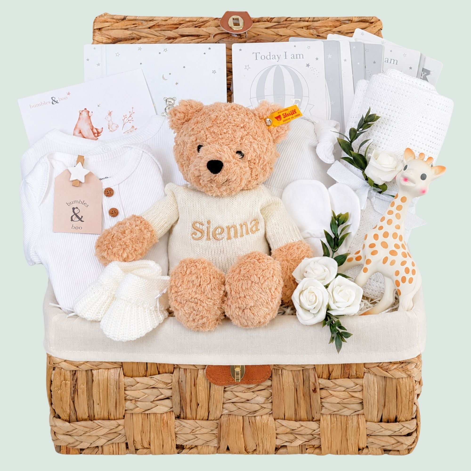 A gifts hamper for a new baby in a seagrass basket with a teddy, baby clothing and other presents. Can be personalised. Bumbles and Boo. 