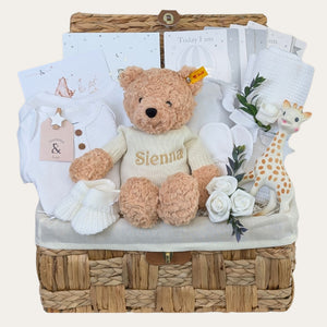 A gifts hamper for a new baby in a seagrass basket with a teddy, baby clothing and other presents. Can be personalised. Bumbles and Boo. 