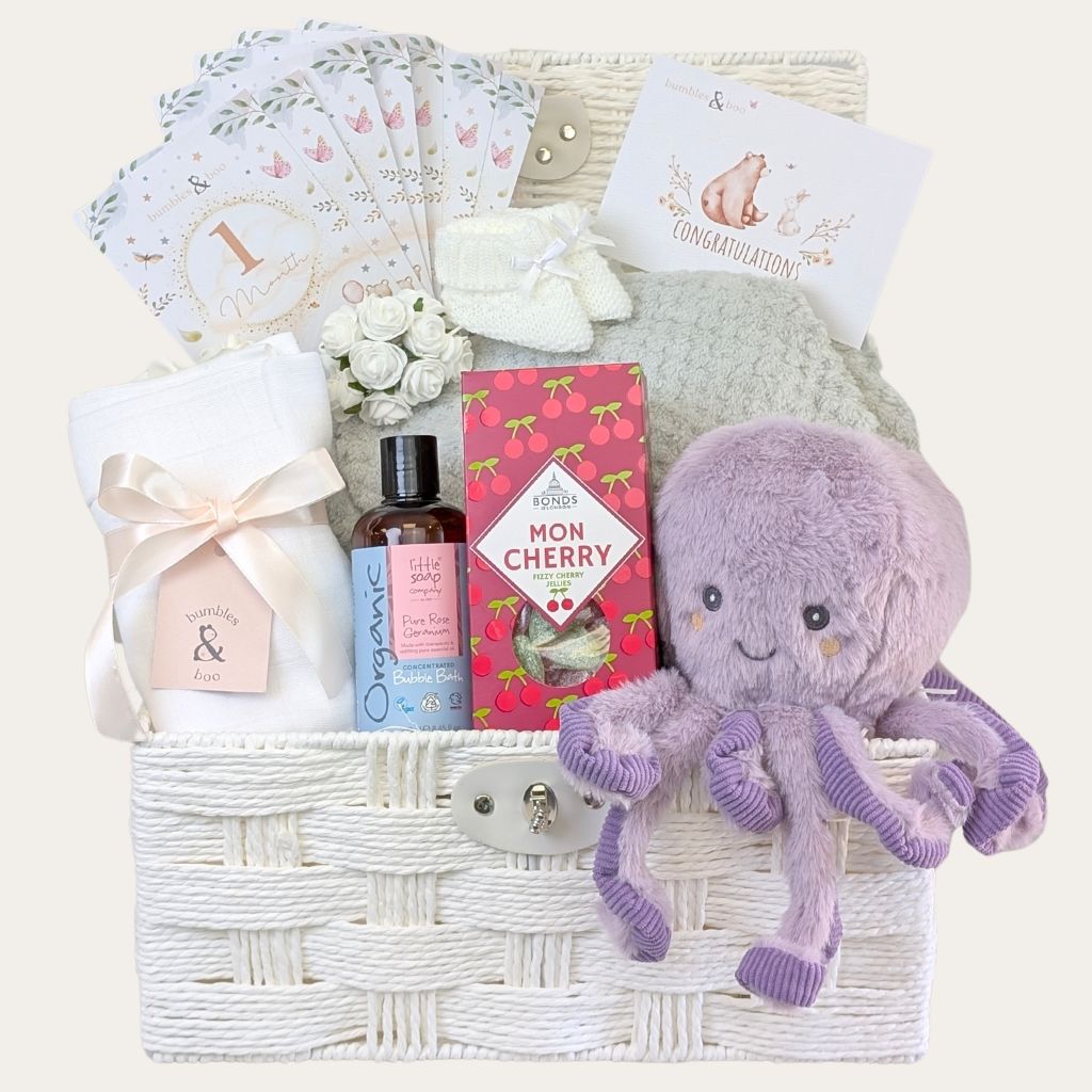 New mum gifts in a white hamper basket with lilac octopus toy, baby blanket, and pampering gifts by Bumbles and Boo.