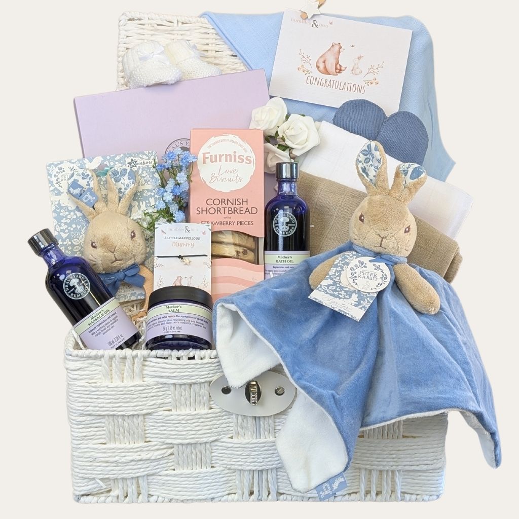 New mum gifts hamper with biscuits, chocolates, Neal’s Yard products and blue presents in a white basket by Bumbles and Boo.