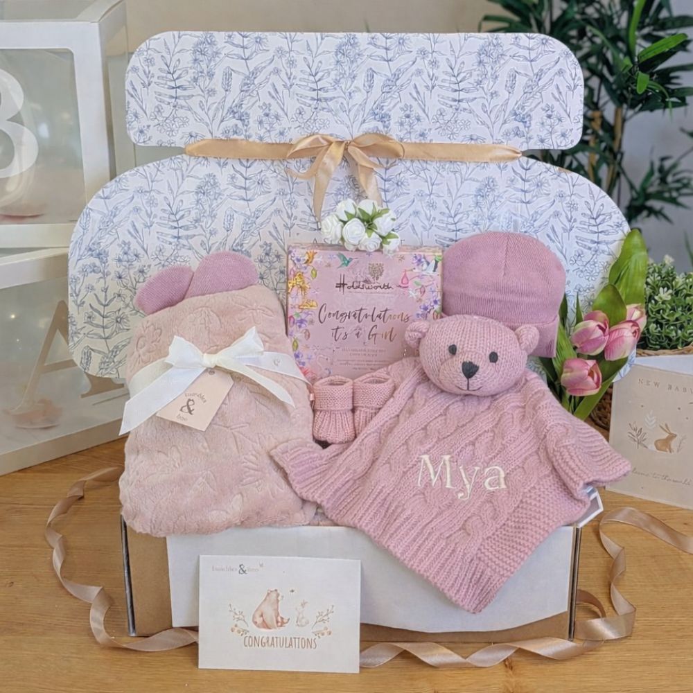Newborn baby girl gifts box with pink presents. Hamper includes pink blanket and newborn comforter