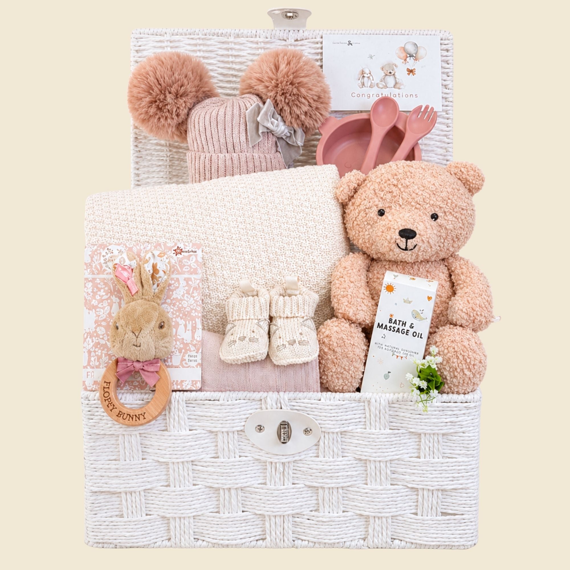 Gifts for a new baby girl in a white hamper basket with teddy bear, knitted hat and cosy baby blanket