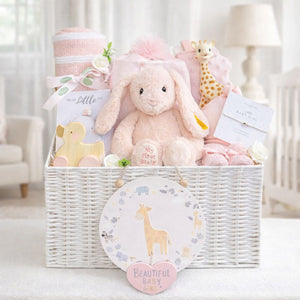 Newborn baby girl hamper basket with gifts including pink steiff bunny, blankets and baby toys in a white basket