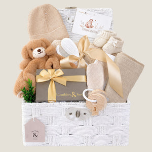 Newborn baby gifts basket with teddy bear, hat, and other items in a white hamper