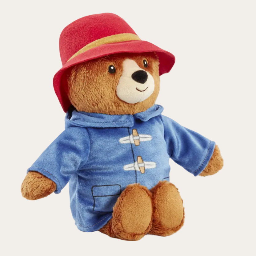 Paddington bear soft toy with red hat and blue coat sitting upright