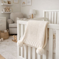 Pale beige knit baby blanket with pom poms.