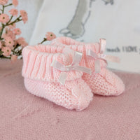 Pale pink knitted baby booties with ribbon bows and folded ribbed cuffs