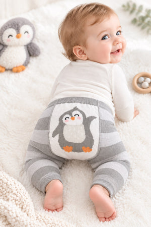 Baby looking back while wearing penguin leggings, with grey stripes, orange penguin feet and ribbed ankle cuffs.