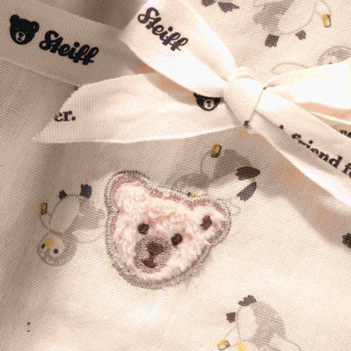 Close-up of the cotton burp cloth showing penguin illustrations, teddy bear embroidery and a tied ribbon.