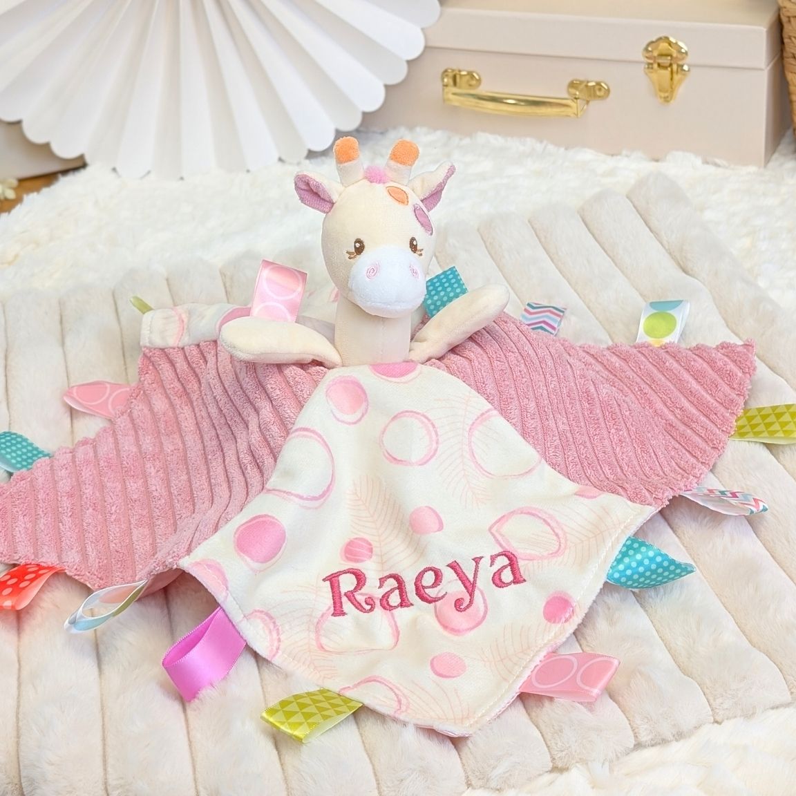 Personalised baby comforter, pink with sensory ribbons and attached giraffe toy embroidered with the name Raeya