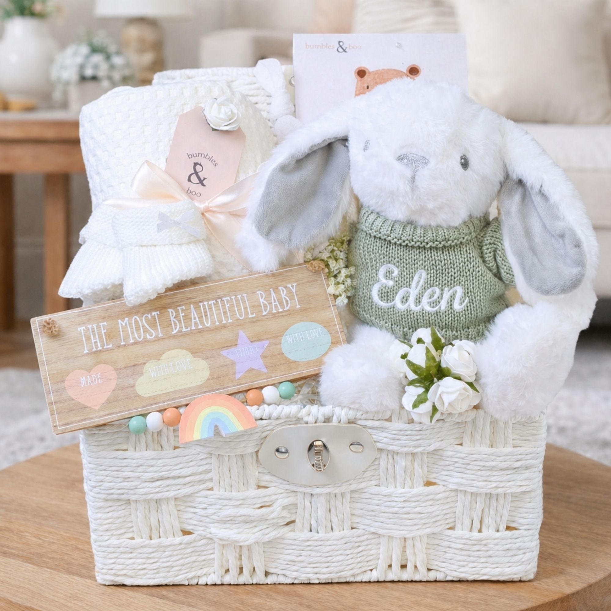 White baby hamper basket full of new baby gifts including bunny, booties and baby blanket.
