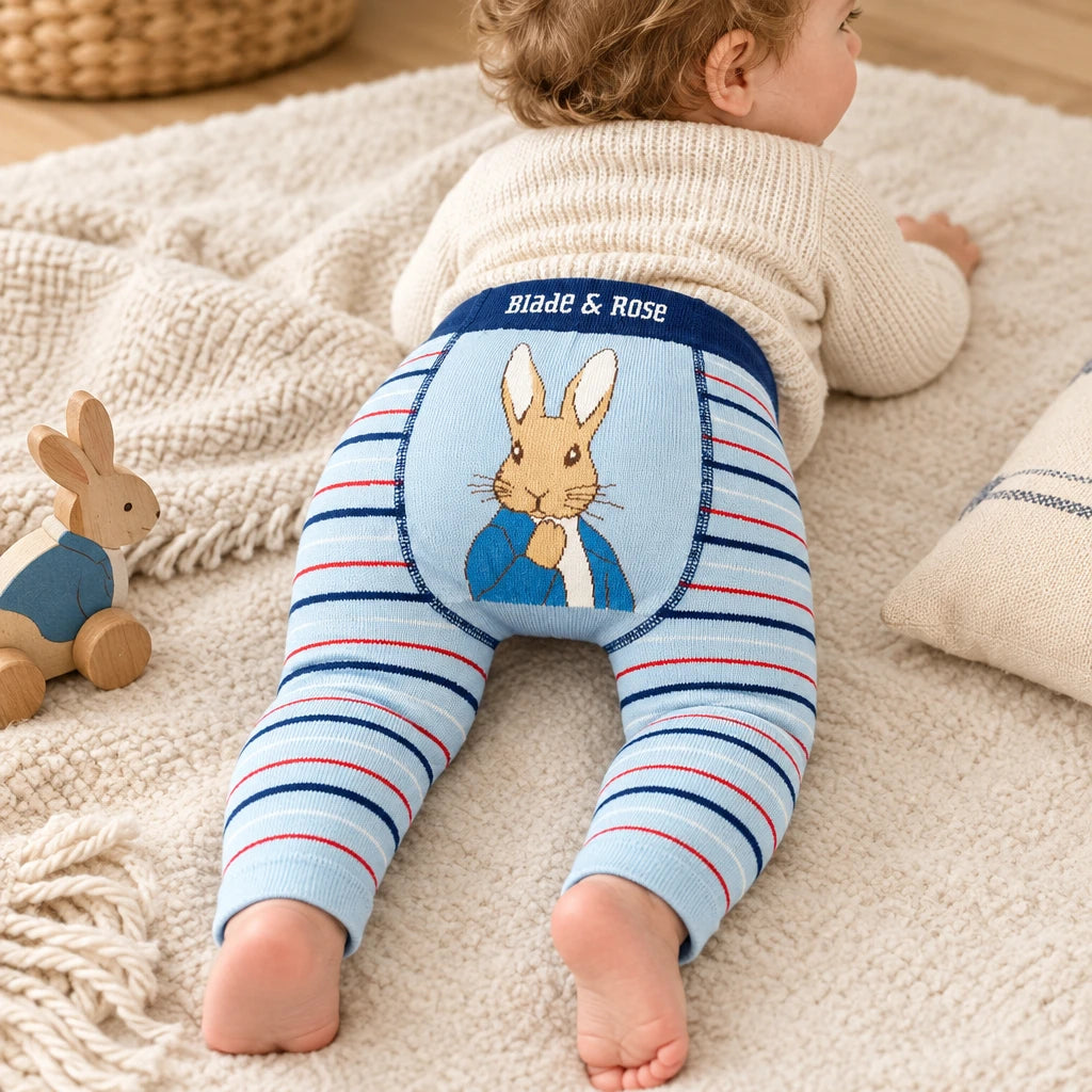 Baby wearing light blue leggings with navy and red stripes and a Peter Rabbit design on the bottom.