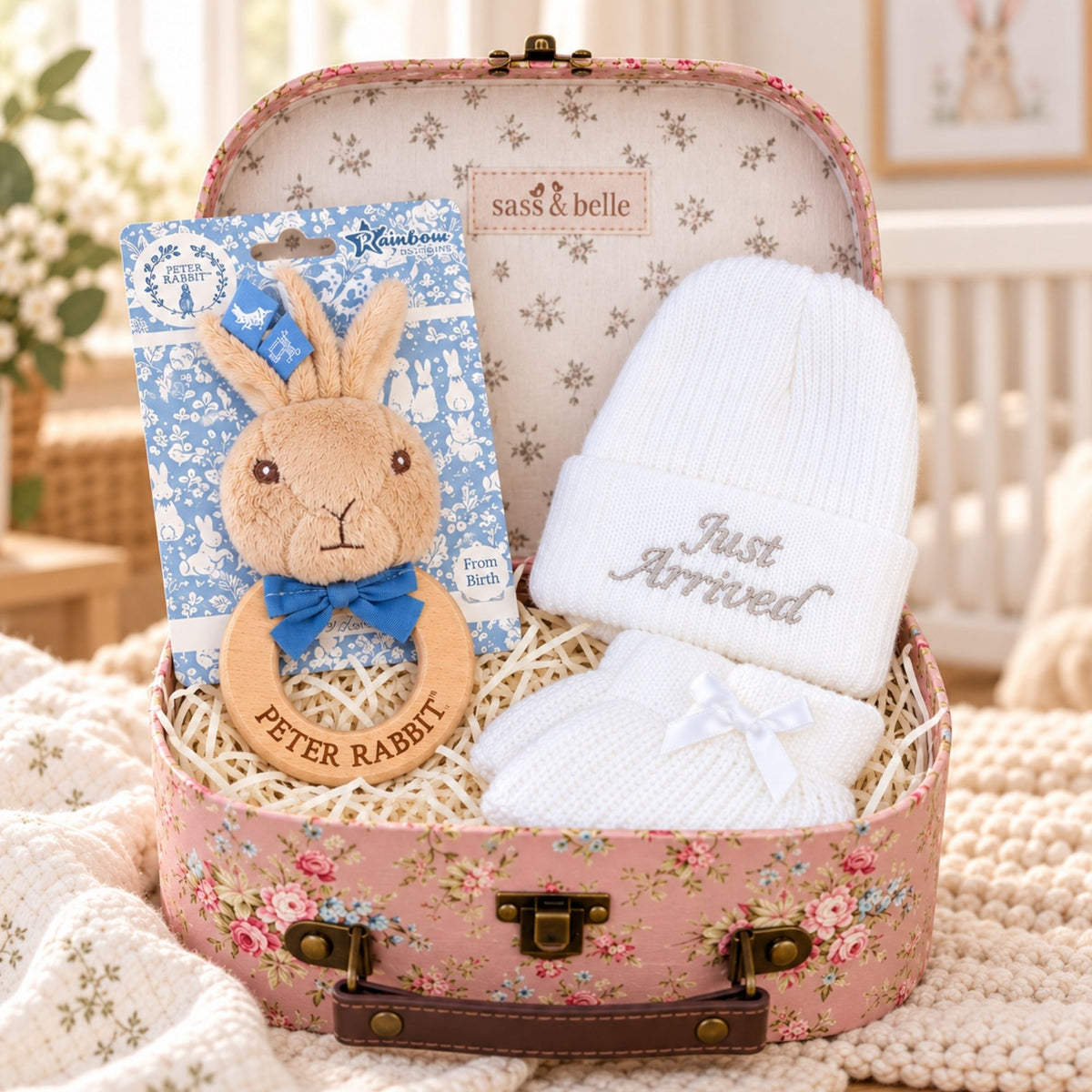 Peter Rabbit new baby hamper in pink floral keepsake suitcase with wooden ring rattle, white Just Arrived knitted baby hat and matching booties.