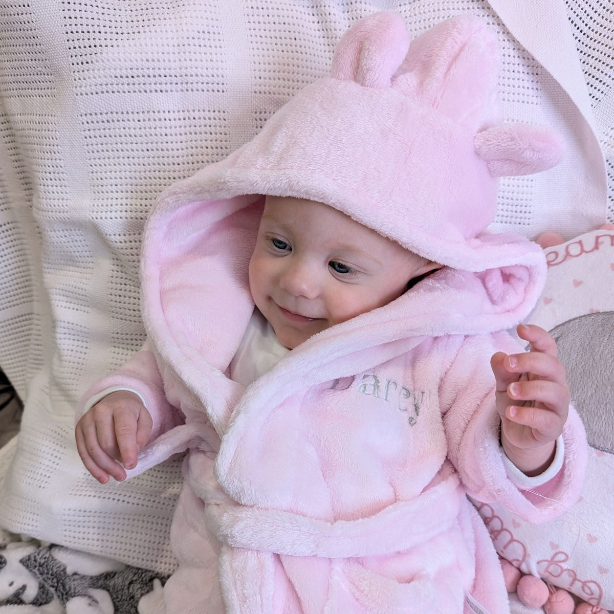 Baby wearing a pink dressing gown with an ear-detail hood and an embroidered name.