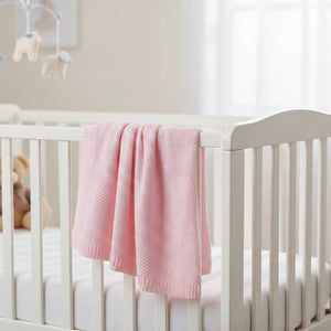 Pink bamboo baby blanket with soft knitted weave displayed flat and draped over a white cot