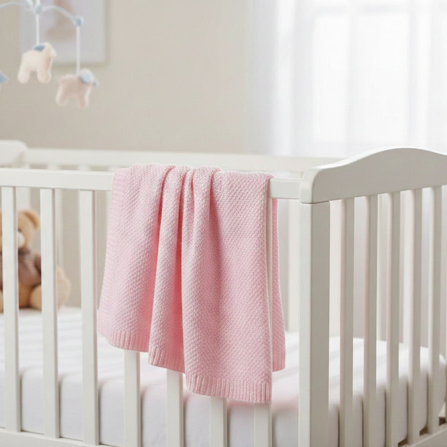 Pink bamboo baby blanket with soft knitted weave displayed flat and draped over a white cot