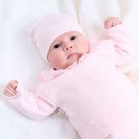 Close-up of a baby wearing the pink knitted hat and bobble top with a white ruffle collar.