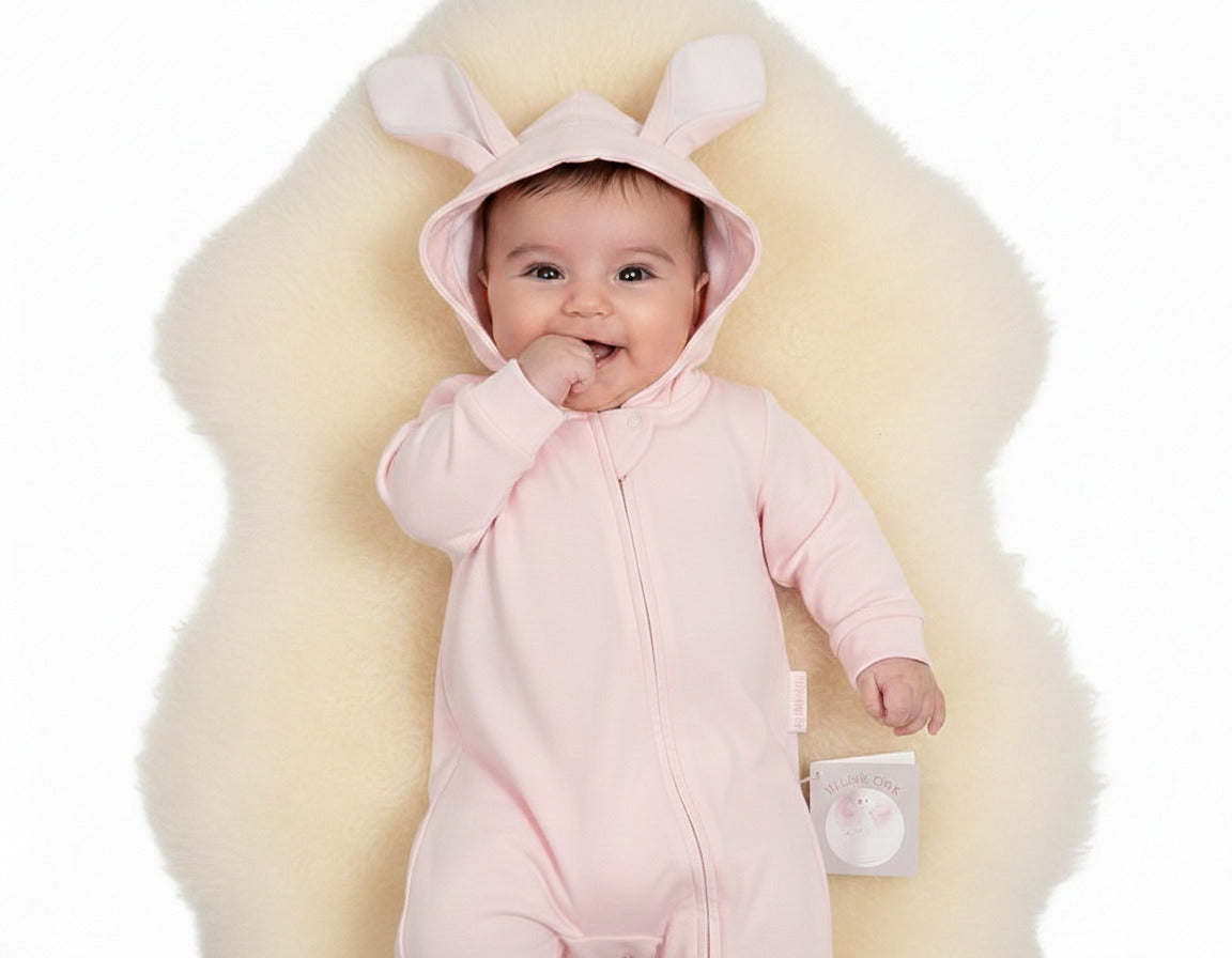 Pink baby sleepsuit with bunny ears hood and zip fastening. Comfortable baby clothes for layering and sleep