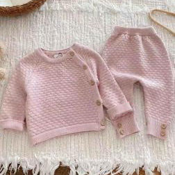 Pink luxury knitted baby clothes set with honeycomb pattern, button fastening top and matching trousers laid fla