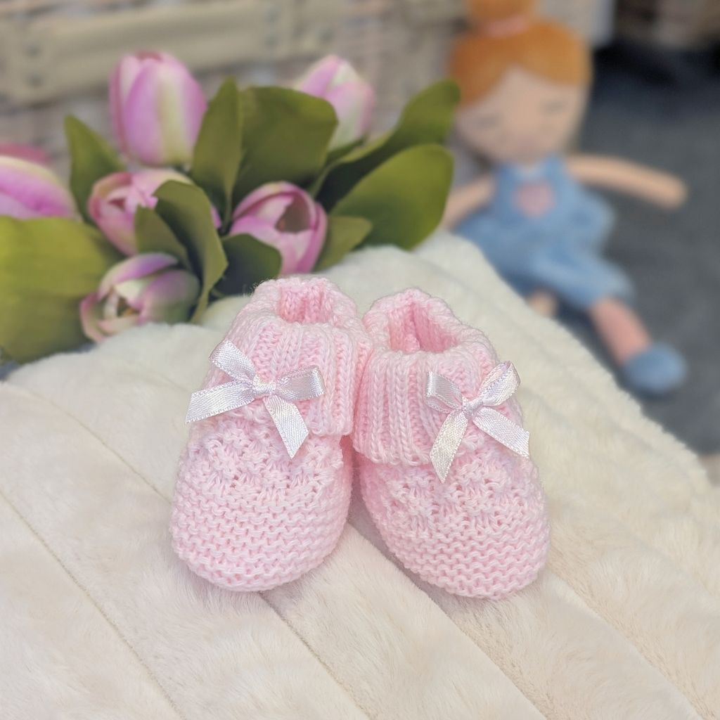 Pink knitted baby booties with little pink bows.