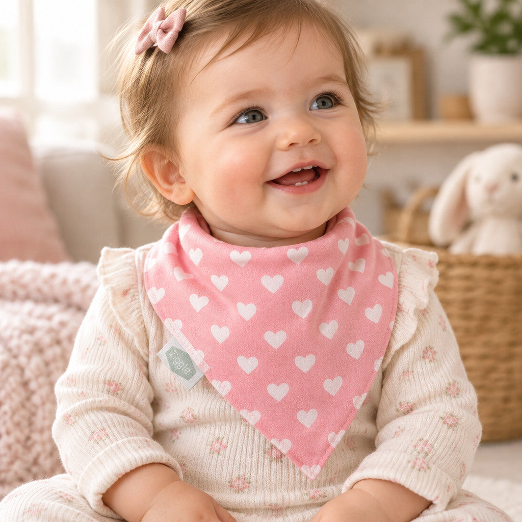 Pink Ziggle bandana dribble bib with a white heart pattern, gathered neckline and white fleece edge.
