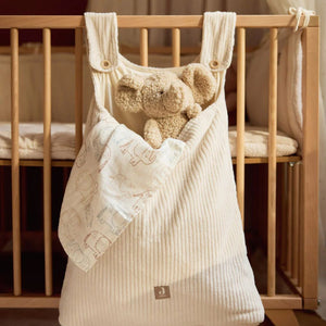 Beige baby bag with elephant teddy plush toy hanging on a wooden crib.