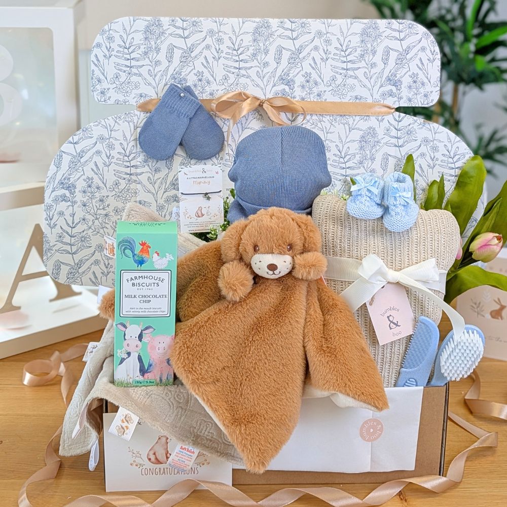 Baby gift basket with teddy bear, blanket, and other items on a wooden surface.