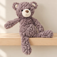 Grey Putty teddy bear with cream muzzle and inner ears sitting on a pale wooden nursery shelf