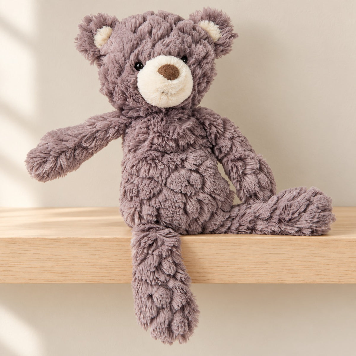 Grey Putty teddy bear with cream muzzle and inner ears sitting on a pale wooden nursery shelf