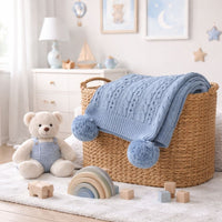 A dusky blue baby boy blanket which is knit and has pompoms. 