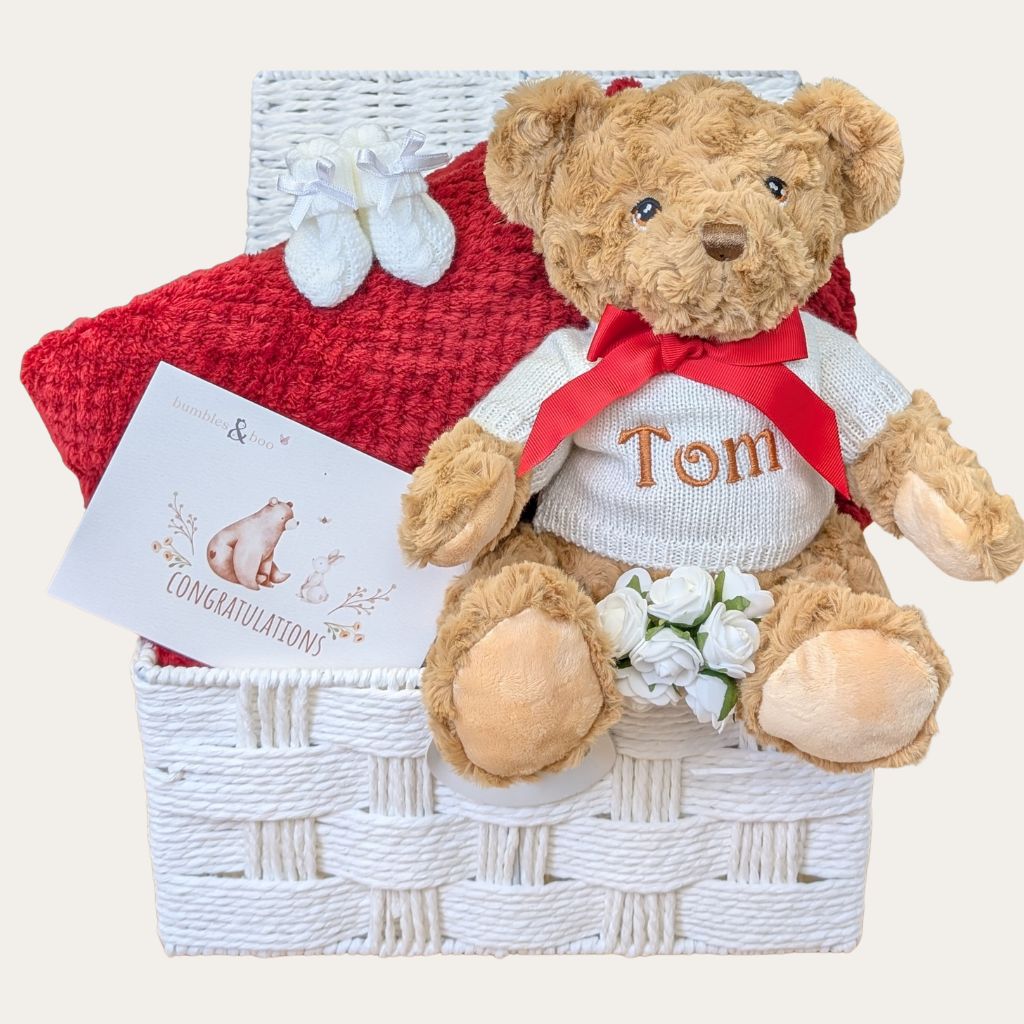 Teddy bear with a sweater and bow tie in a baby gift basket.