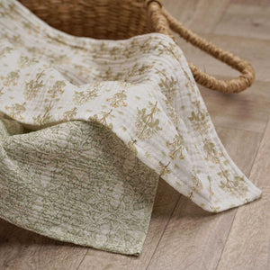 Two sage and cream patterned baby muslin cloths draped beside a woven basket.