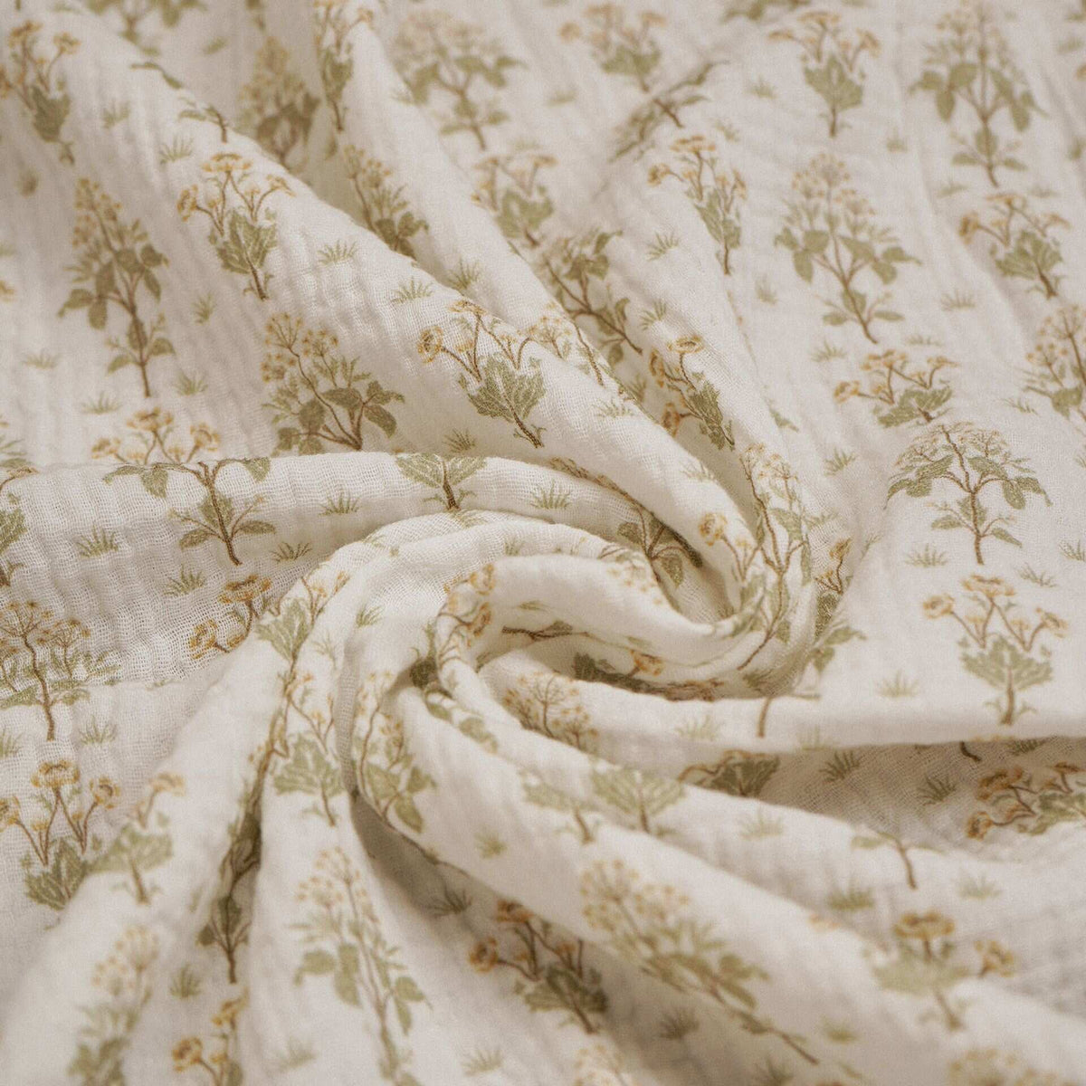Close-up of cream baby muslin fabric with sage floral sprigs arranged in soft folds.