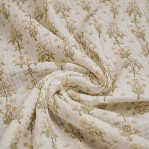 Close-up of cream baby muslin fabric with sage floral sprigs arranged in soft folds.