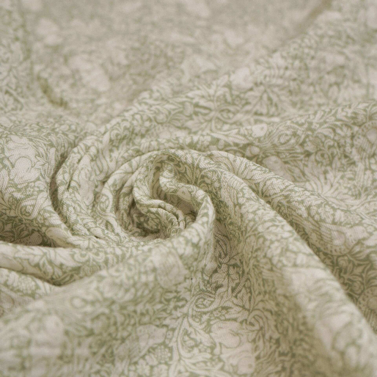 Close-up of sage green baby muslin fabric with an intricate leafy pattern.