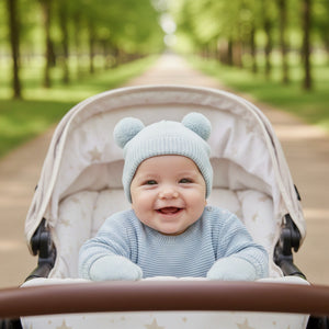 Baby in a stroller wearing a sage green knit hat with pom pom bear ears