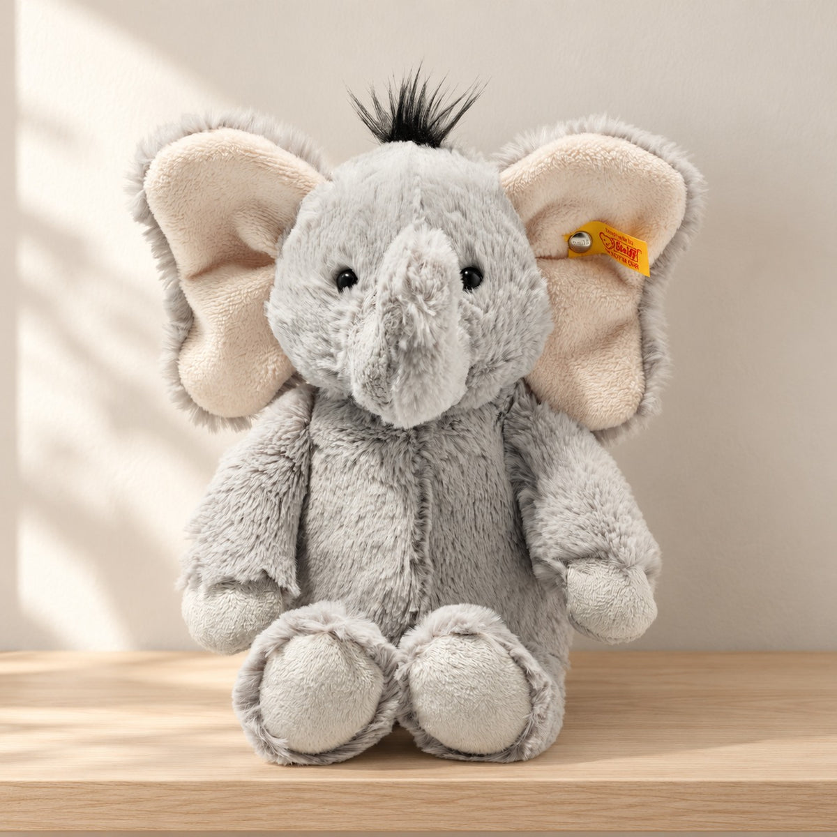 Steiff Ella grey elephant with large pale inner ears and a black hair tuft sitting on a wooden nursery shelf