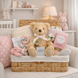 presents for a baby girl in a hamper basket and includes a teddy bear and biscuits for the new parents.