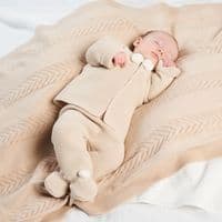 Full outfit view of a baby in the taupe jacket and footed leggings with ivory pom pom details.