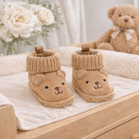 Pair of taupe knitted baby booties with embroidered teddy faces, small ears and folded cuffs.