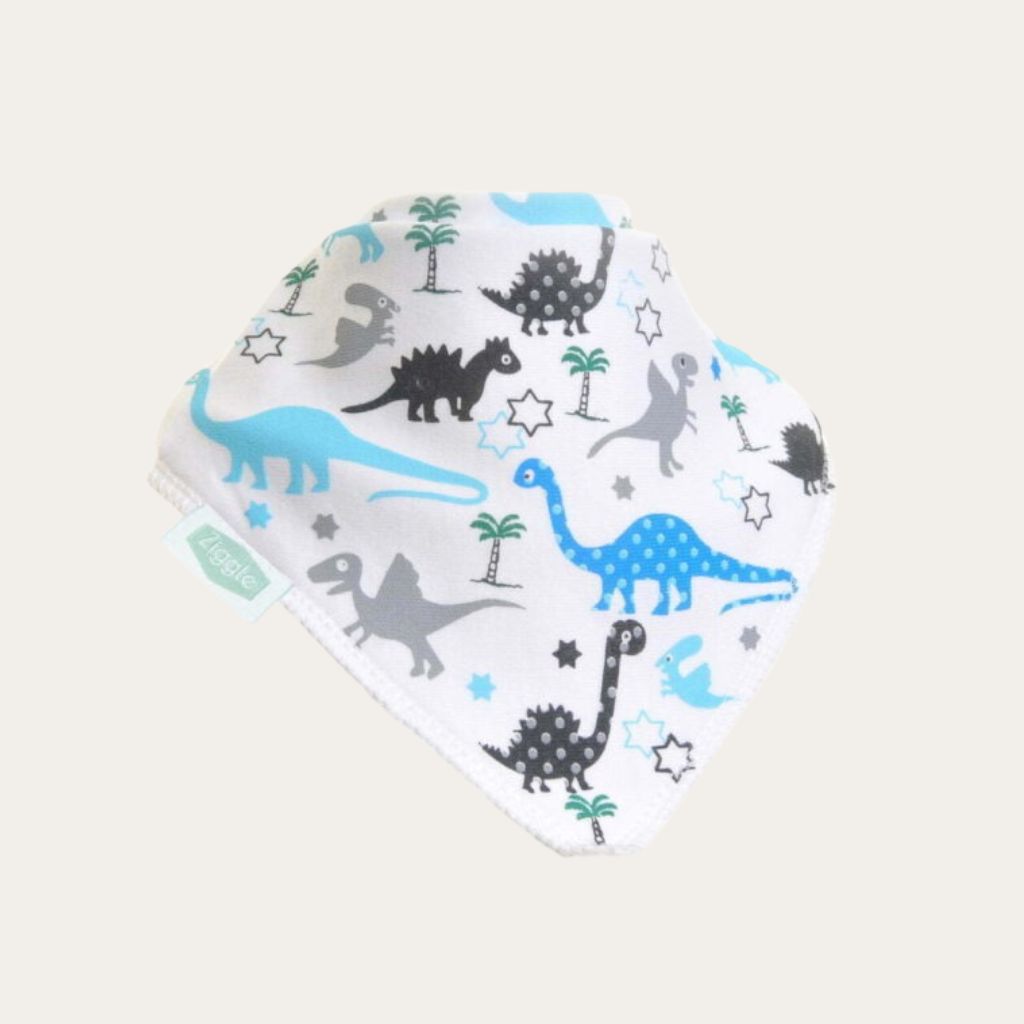 White bandana baby bib with blue, grey and black dinosaurs and small green trees, shown on a pale background.