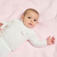 Close-up of a baby in the white pom pom cardigan, showing its crossover front and trimmed edging.