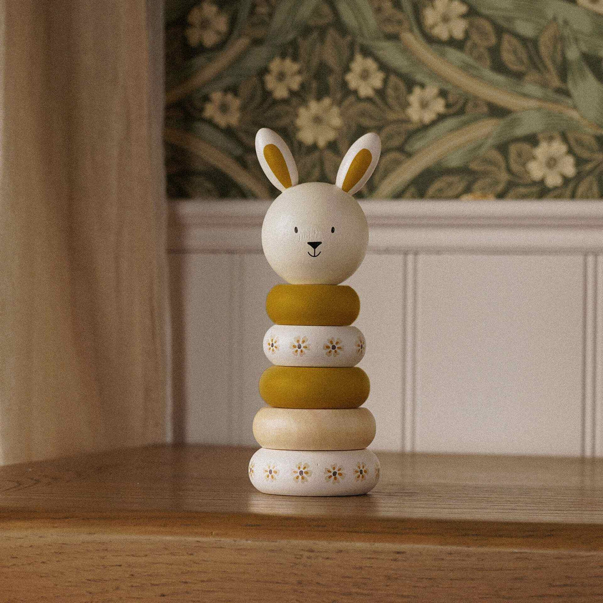 Wooden bunny stacking toy with ochre and floral cream rings displayed on a wooden cabinet.