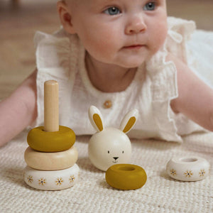Child beside the partly assembled bunny stacker, with its head and loose rings on a knitted blanket.