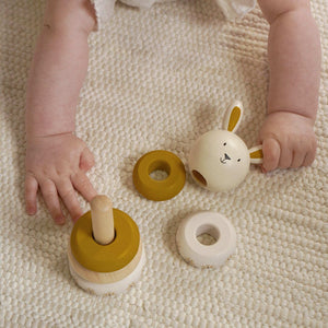 Child’s hands arranging the wooden bunny head and stacking rings on a knitted blanket.