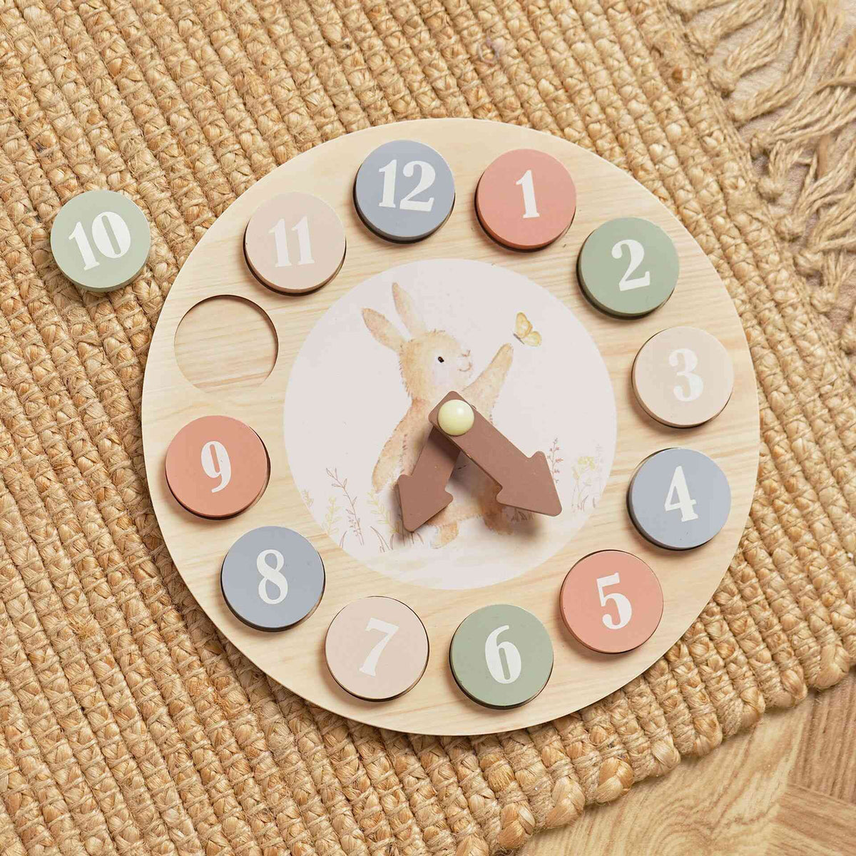 Wooden learning clock on a woven mat with the green number 10 disc beside it