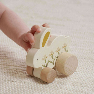 Child’s hand holding a cream floral wooden bunny toy by its ear on a knitted blanket.